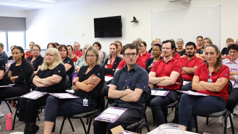 Members at Ramsay Health Care sit at a meeting with crossed arms and stern looks on their faces.