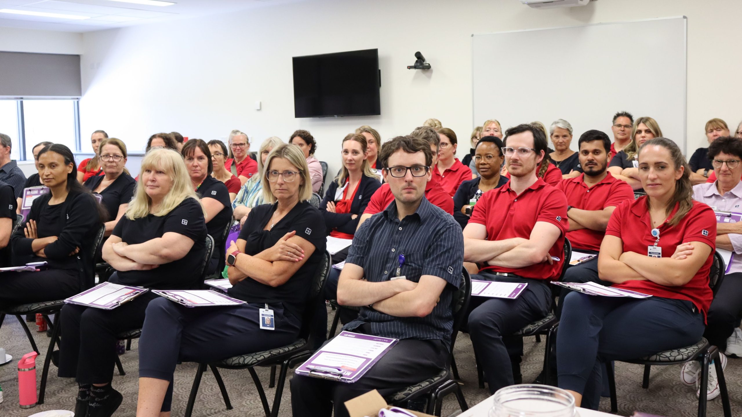Members at Ramsay Health Care sit at a meeting with crossed arms and stern looks on their faces.