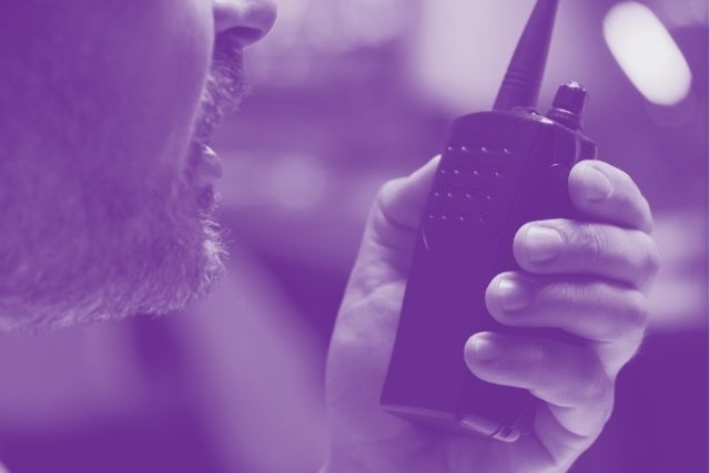 A monochromatic image of the close up of a security officer's mouth near a hand held radio.