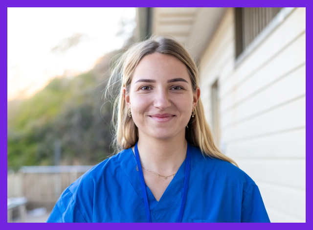 Blonde, female health worker in blue scrubs, smiling.