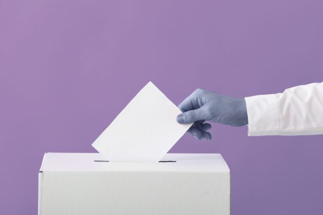 A hand posting a ballot into a ballot box on a mauve background