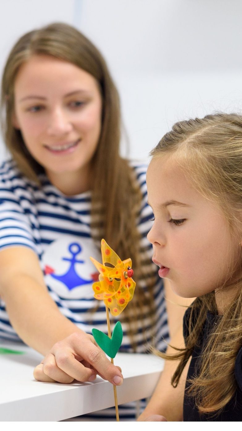 A speech pathologist working on an exercise with a child using a pinwheel.